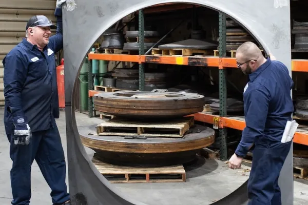 Technicians maneuver a large spun metal ring inside a fabrication shop